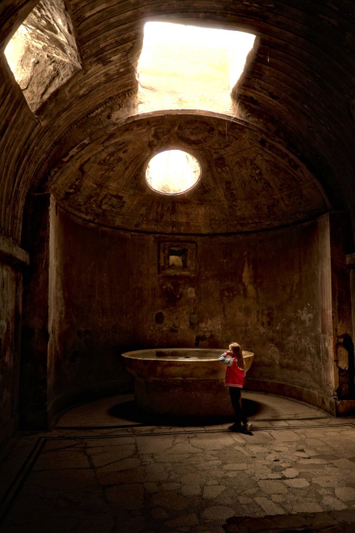 Come un'apparizione una bambina si ferma assorta ad osservare le rovine delle terme di Pompei