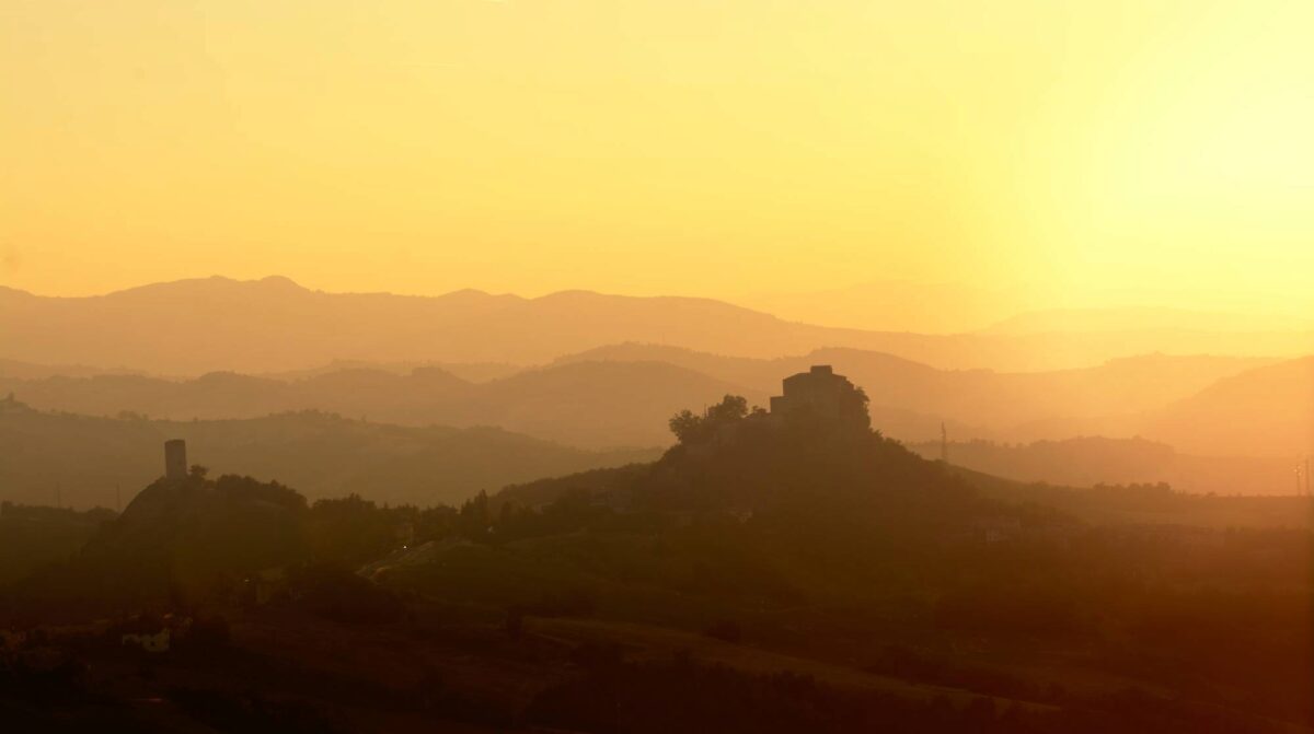Il castello di Rossena si staglia imponente dalla cime della rupe. A sinistra la sempre fedele torre di Rossenella. Il pulviscolo sospeso nell'aria calda della sera riflette la luce del sole che tramonta donando alla scena l'aspetto di un dipinto.