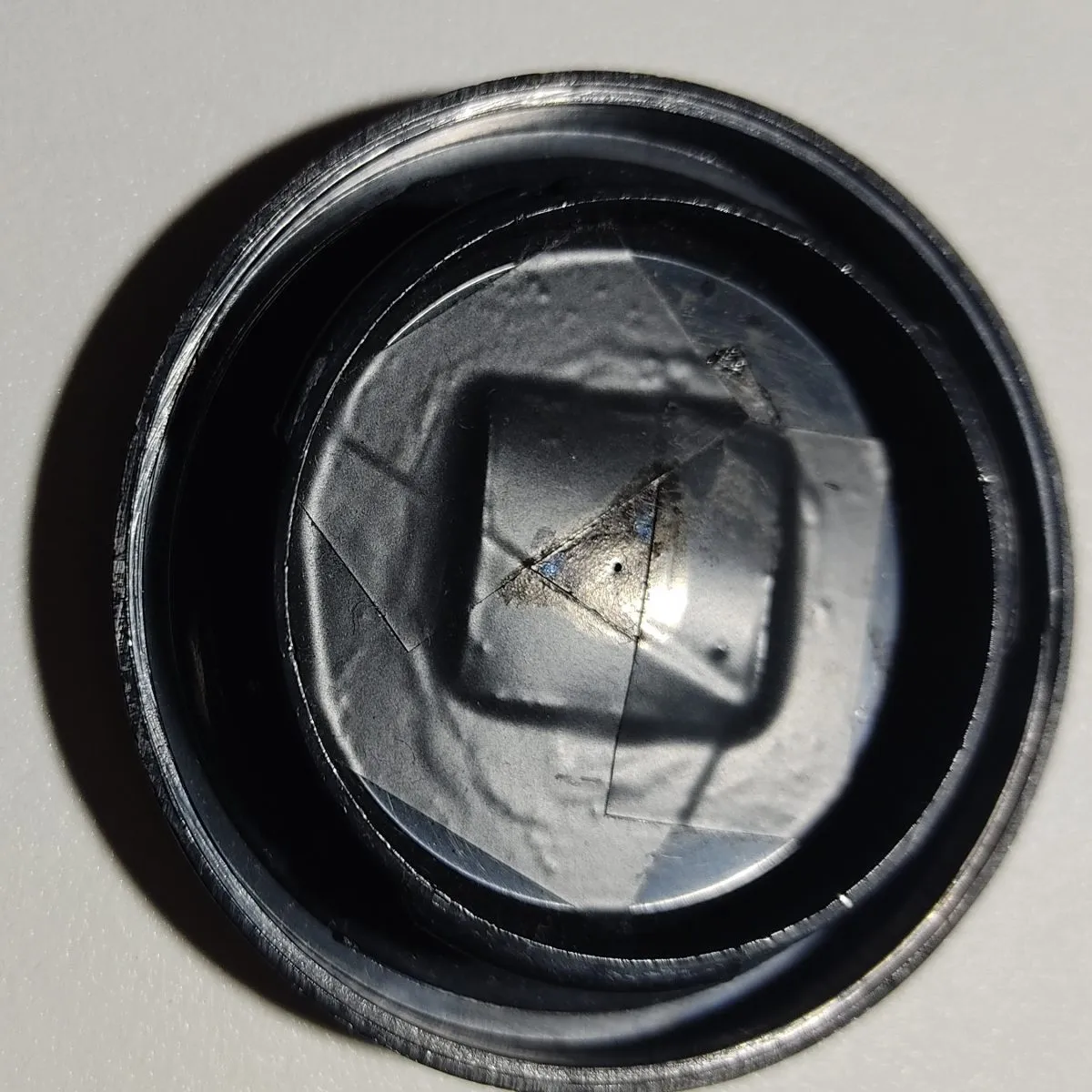 Il lamierino è attaccato sul retro del tappo con colla e nastro isolante da elettricista (di colore nero e con superficie opaca). Si vede chiaramente il forellino.
